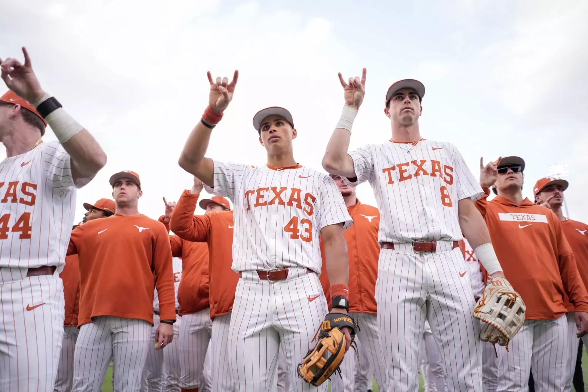 Texas Longhorns baseball players in white pinstriped uniforms making Hook 'em Horns gesture